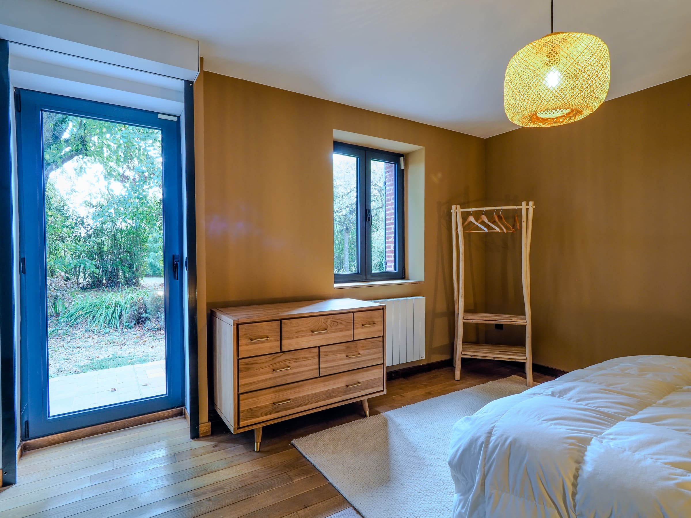La Chambre Deluxe, sa porte-fenêtre sur le jardin, sa commode et son portant en bois