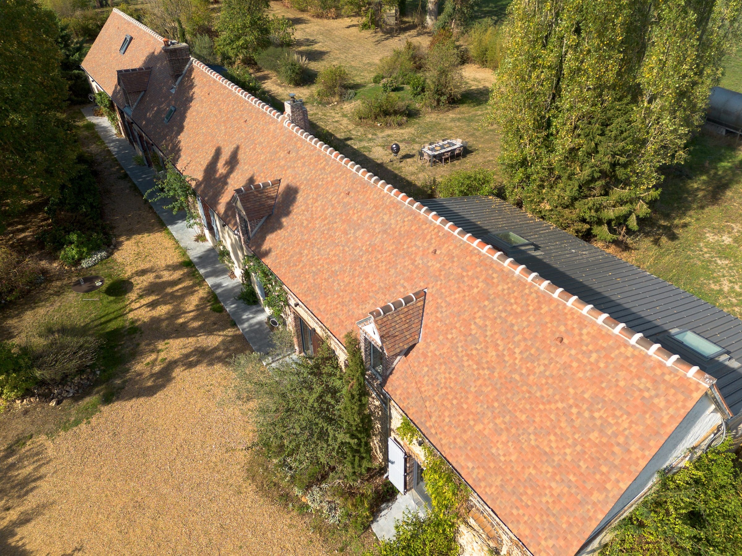 La longère vue du ciel, son toit de tuiles plates et ses lucarnes