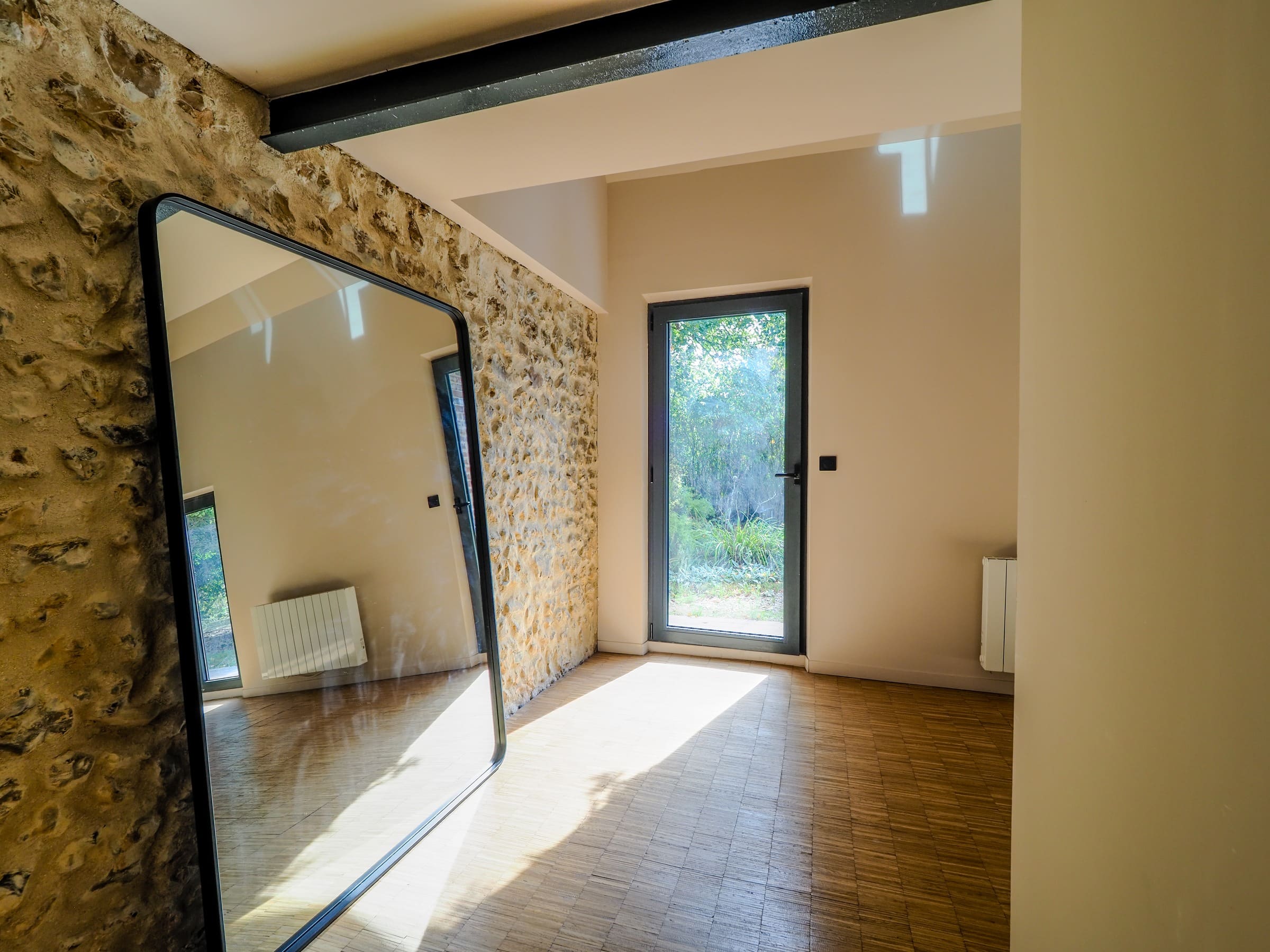 Le mur de silex et le grand miroir, près d’une porte vitrée ouverte sur le jardin