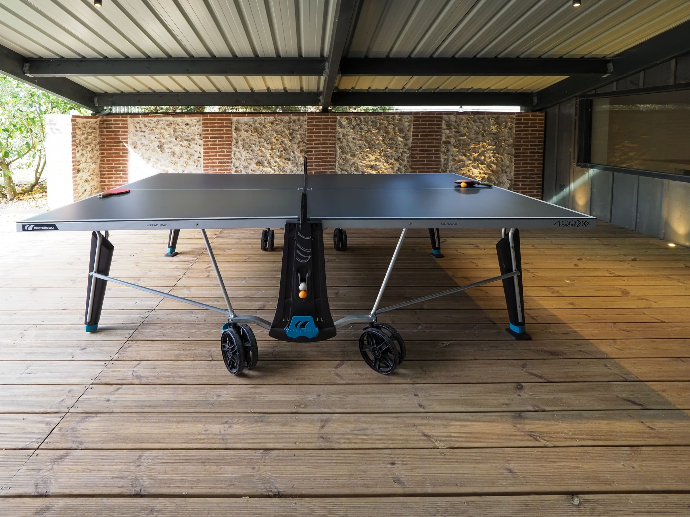 La table de ping-pong sous la terrasse couverte, devant le mur de silex et de brique