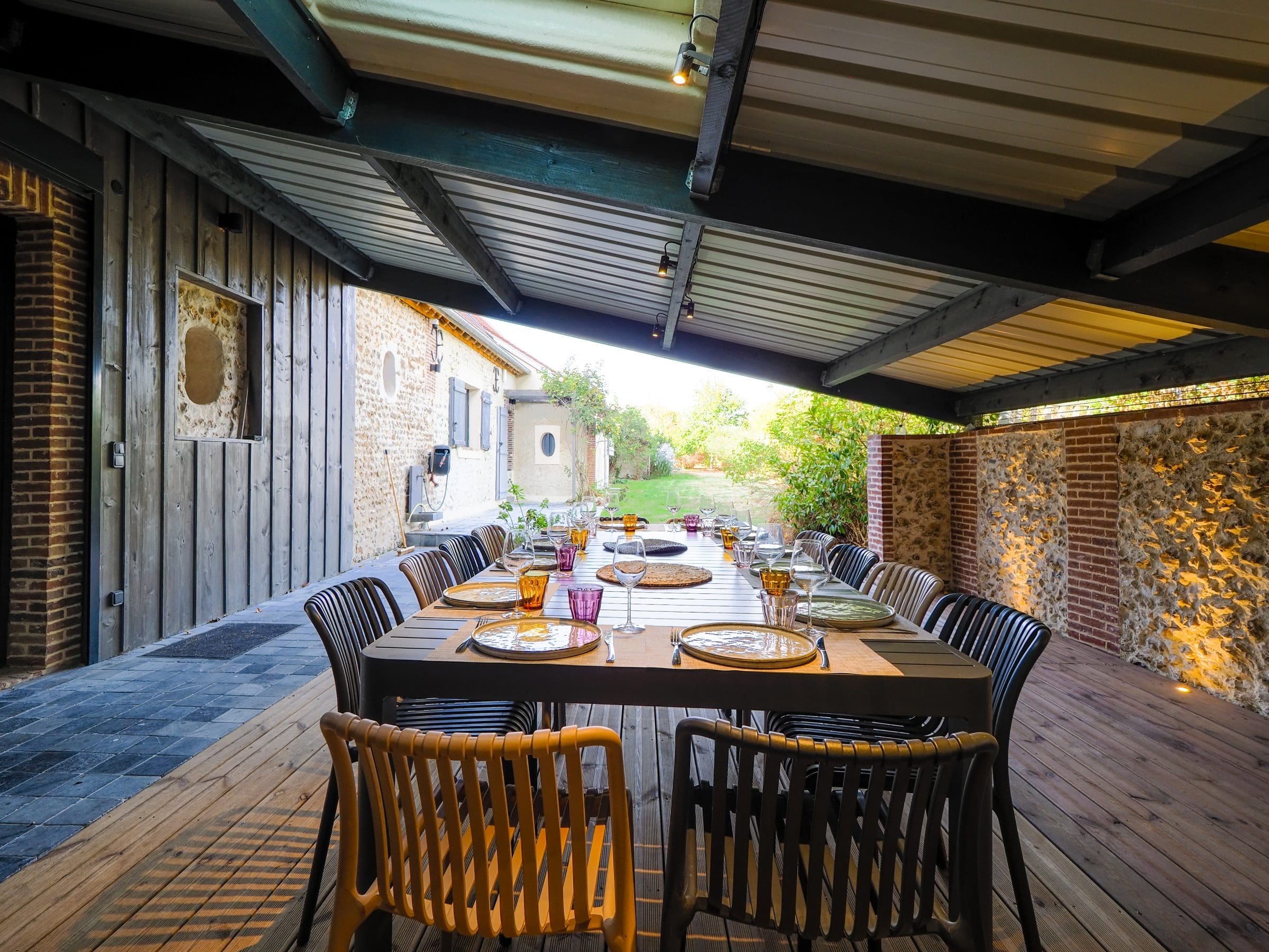 La table de douze dressée pour le dîner sous la terrasse couverte, le mur de silex éclairé